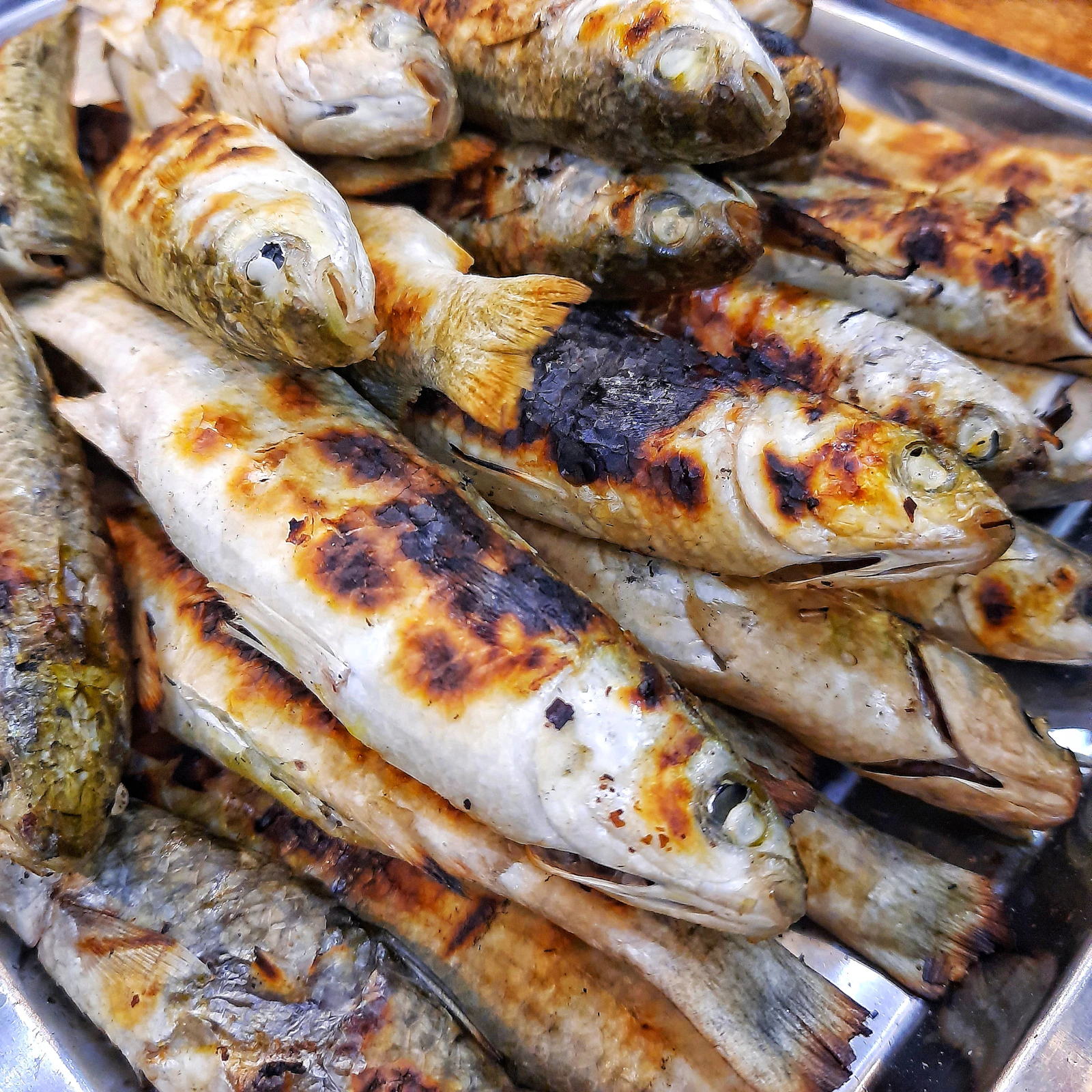 Grilled sardines on a metal plate in a traditional tasca