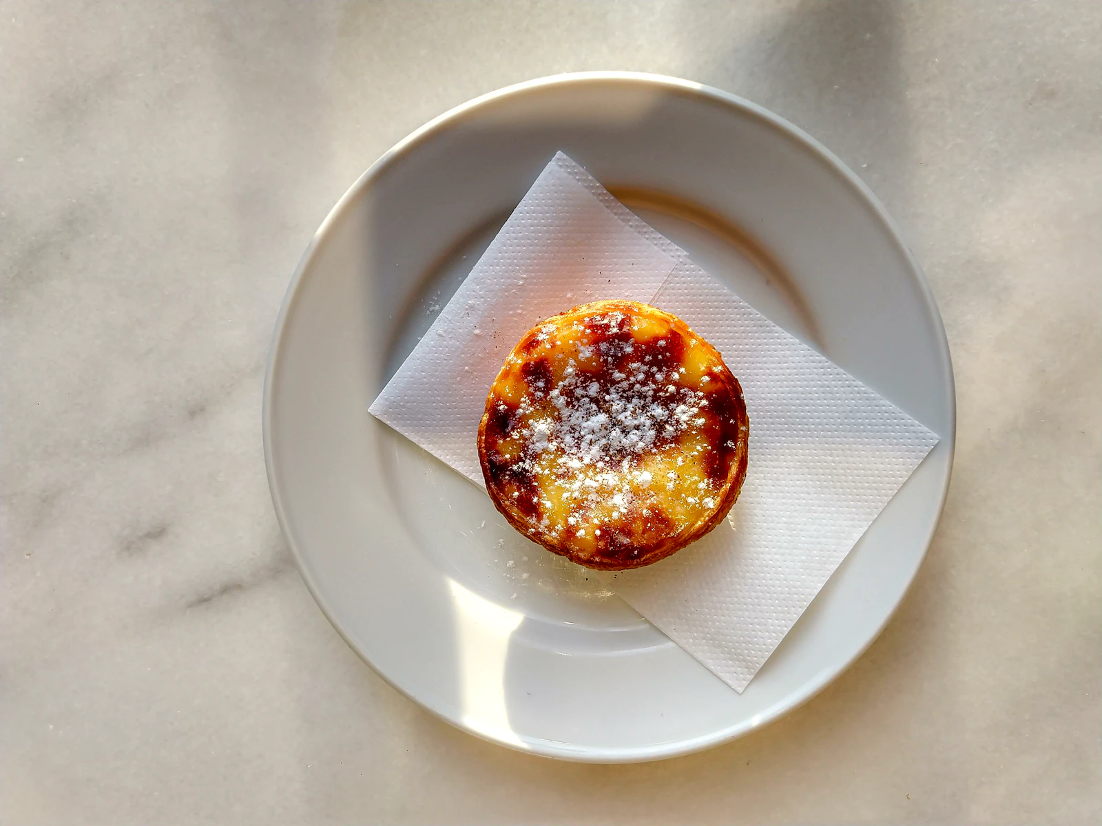 Pastel de nata on a small ceramic plate with espresso